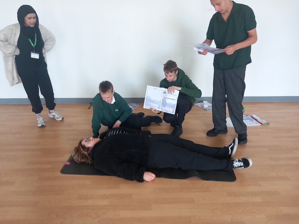 Pupils practicing first aid on a member of staff who is laying on a mat on the floor